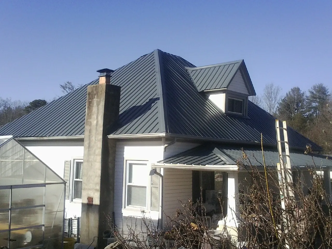 Dark blue standing seam metal roof on a white farmhouse with dormer — Slate & Tile Roof Repair by Roofing Brothers in Vernal