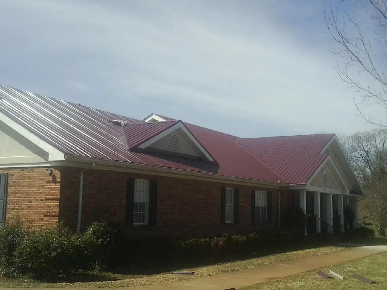 Red metal roof with gabled entries on a long brick building, from a Hail Damage Roof Repair job in Vernal