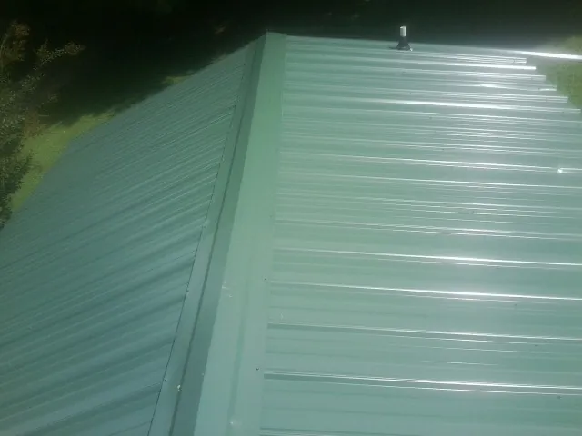 New green metal panels meeting at the ridge of a roof — Flat Roof Repair work by our crew in Vernal