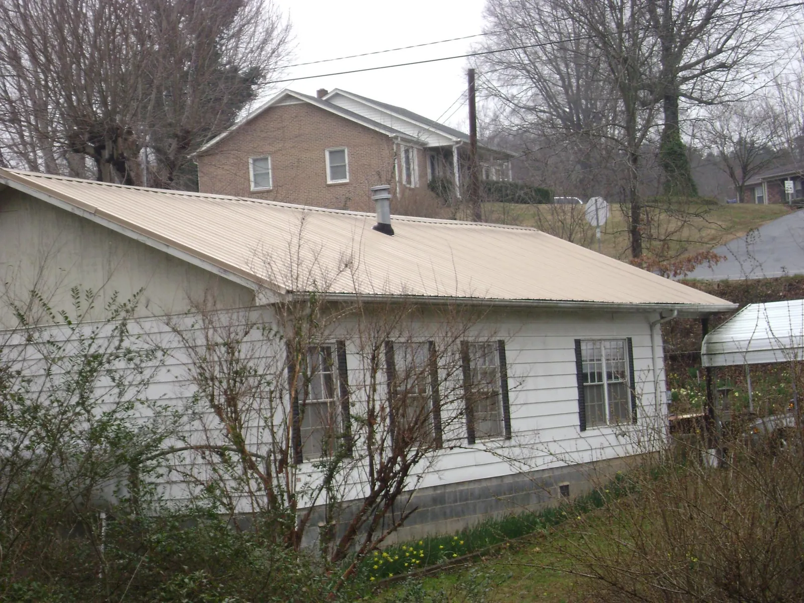 Tan metal roof on a white sided house set into a hillside — Commercial Roofing by Roofing Brothers in Vernal